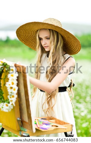 Blonde girl in field of daisies paints a picture