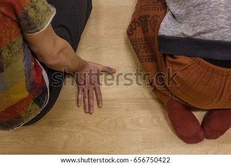 two dancers sit on floor, One of them rests on the palm of your hand, back view