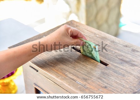 Hand Putting Money Into a Wooden Donation Box Royalty-Free Stock Photo #656755672