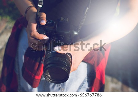 Close-up of female hands holding a professional camera. Female photographer with a professional camera. Lens flare in the background.