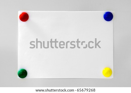 White paper hanging on grey background with four magnets colored blue, red, green and yellow
