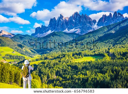 Elderly woman - tourist with backpack takes pictures in the Val de Funes. Warm autumn in Tirol, Dolomites. The concept of active and ecotourism