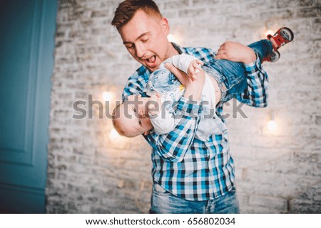 Picture of laughing dad and son dressed in plaid shirts.On the background of a brick wall and beautiful lamps