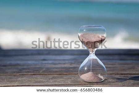 Sand running through the bulbs of an hourglass measuring the passing time in a countdown to a deadline. Beach and sea background, concept for vacation countdown. Time for relaxation. Royalty-Free Stock Photo #656803486