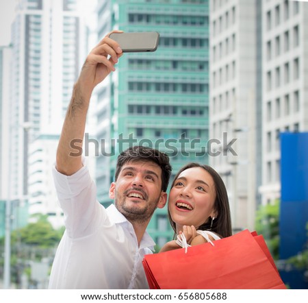 Loving couple taking photo in shopping,Happy couple using smart phone during the shopping,Portrait of smiling couple with shopping bags in the city.Two girls with paperbags selfie during shopping,
