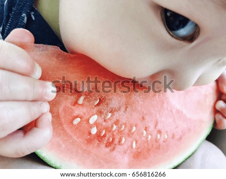 Cute 7 month old asian baby boy is eating watermelon
