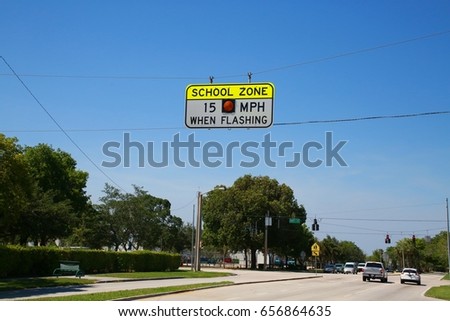 School Zone 15 Mph When Flashing Sign with Black Letters on Yellow and White Background Without Light Lit against Clear Blue Sky Close to Traffic Intersection