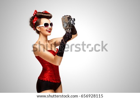 Retro photo of a pin-up girl with an old vintage 8 mm camera on grey background.