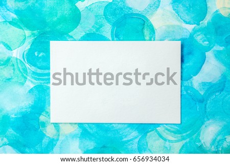 An overhead photo of a blank white business card on a teal blue watercolor texture. A mockup or a minimalist banner with copyspace