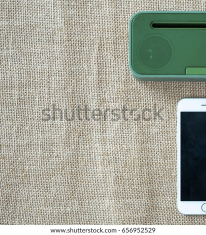 Green portable speaker and white smartphone on sackcloth background.