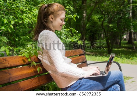 student working with a laptop sitting in a bench in a park