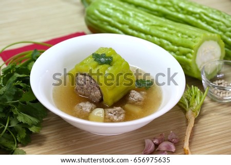 Bright shot. Bitter gourd ring filled with seasoned minced pork in clear soup with garlic, coriander roots, white peppercorn and ingredients on wooden table.
