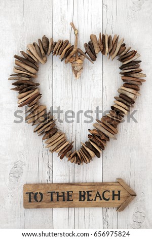 Rustic driftwood heart with wooden to the beach sign on distressed rustic white wood background.