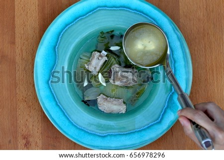 Pickled mustard leaves with pork ribs clear soup, with a hand ladle pouring broth into the bowl
