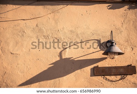 Wall at sunset light with a street lamp and wooden sign.