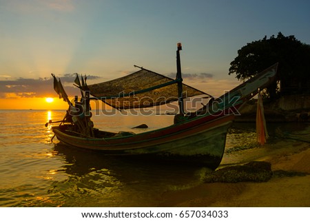 SILHOUETTE MUSLIM FISHERMAN LONG-TAIL BOAT AT ISLAND BEACH ANCHORAGE IN EVENING , DRAMATIC TWILIGHT SKY BACKGROUND