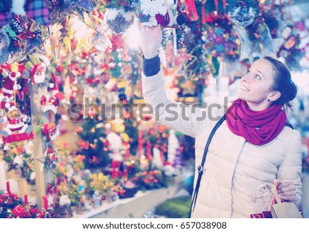 Portrait of excited smiling young woman choosing gifts and decorations at Christmas fair in evening
