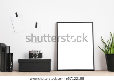 Stylish and modern workspace with black empty frame, sticky notes, books and camera on home or studio.