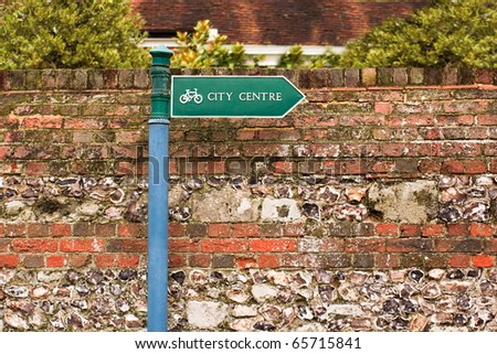 A city centre sign indicating a cycle route against a brick and flint stone wall