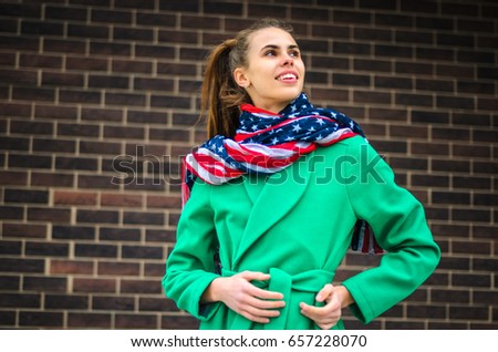 a young girl dressed in a green coat and yellow dress. Pure colors in the photo. girl fun fooling around . against a brick wall