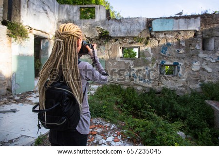 Young woman with blonde dreadlocks takes pictures of Abandoned buildings.