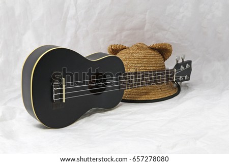 Weave hat and black ukulele on the white background. ukulele is a small four-stringed guitar of Hawaiian origin.