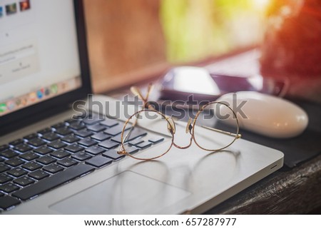 Eyeglasses on laptop keyboard with smartphones on wooden table at evening, close up