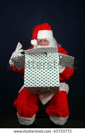 Santa Claus holds a christmas present he is going to give to some lucky boy or girl for Christmas as he sits in a chair