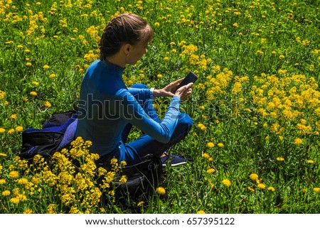 Woman holding mobile phone on the lawn of yellow flowers.
