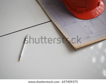 In selective focus of pen and orange safety helmet on blur stack blueprints in engineer architecture workplace. (Awaiting contractor sign contract)