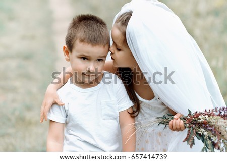 Young bride and groom playing wedding summer outdoor. Children like newlyweds. Little girl in bride white dress and bridal veil kissing her little boy groom, kids game. Bridal, wedding concept.
