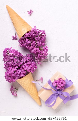 Splendid lilac flowers in waffle cones in box with present  on grey textured background. Top view. Vertical image.