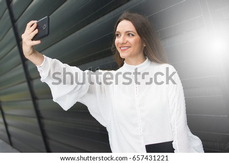Portrait of smiling pretty young business woman taking a selfie. Modern business woman on the company ground. Outdoor break.
