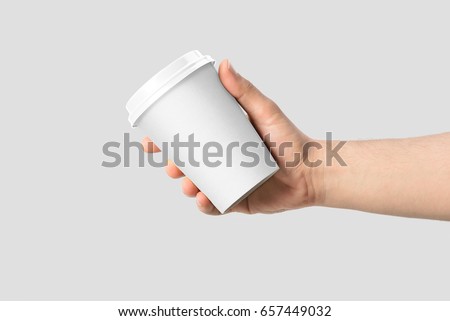 Mockup of male hand holding a Coffee paper cup isolated on light grey background.  Royalty-Free Stock Photo #657449032