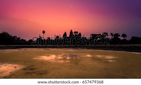 Silhouetted photo of the main temple of Angkor Wat at dawn, with the moon above. 