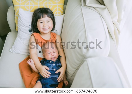Little sister hugging and kissing her newborn brother.Toddler kid meeting new sibling. Cute girl and new born baby boy relax in a sofa.Family with children at home. Love, trust and tenderness.