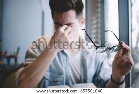 Close up portrait of an attractive man with eyeglasses. Poor young guy has eyesight problems. He is rubbing his nose and eyes because of weariness Royalty-Free Stock Photo #657501040