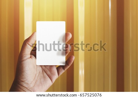 Hand holding Blank business card for mock up, present over yellow gold background, Warm tone filter