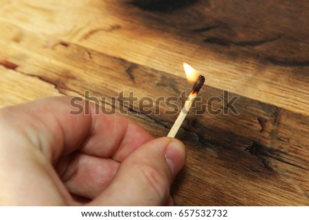 A man holding a lit match. This image also contains a wooden background and can be used to represent fire starting or arson.  Royalty-Free Stock Photo #657532732
