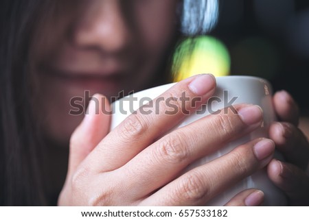 Closeup image of asian woman holding and drinking hot coffee with feeling good and smiley face