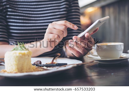 A woman using smart phone with cake and coffee cup on wooden table in restaurant 