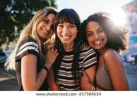 Three beautiful smiling girl friends standing together. Multi ethnic group of women outdoors in the city looking happy. Royalty-Free Stock Photo #657584614