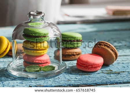 Green, pink and yellow french macarons under the glass on the wooden boards, soft focus background