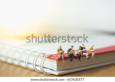 Reading, study and hobby concept. Group of businessman miniature sitting and reading newspaper and book on circle notebook.