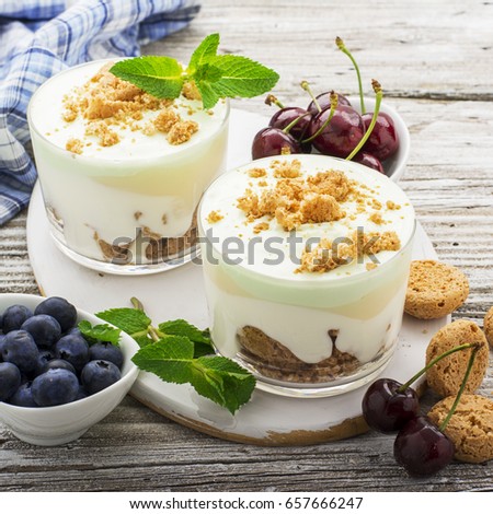 Healthy summer dessert of berry yogurt almond cookies portioned in glass cups on a light wooden background with ripe blueberries and juicy cherries. Selective focus. the concept of fitness nutrition.
