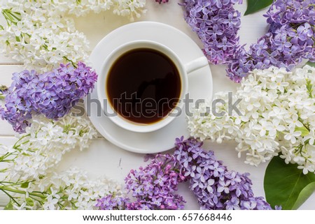 Background with branches of lilac in different colors - white, lilac and purple on a white-painted wooden boards and a Cup of black coffee Top view  The theme of spring, summer, good morning