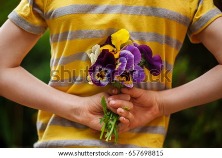 Child hands holding a bouquet pansies flower . Focus for flowers. Back view.