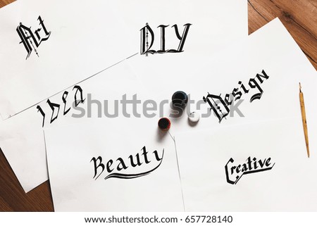 Sheets of paper with inspirational words drawn with ink. Top view. Painter workshop, business inspiration, calligraphy, creativity concept