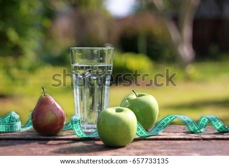 A glass of water, measuring tape and apples on on bright nature background. Healthy life, diet and healthy food concept.