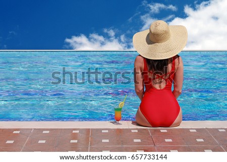 Back view of beautiful woman in bikini and large hat relaxing at pool with cocktails. Summer holidays, travel, vacation concept. Copy space.